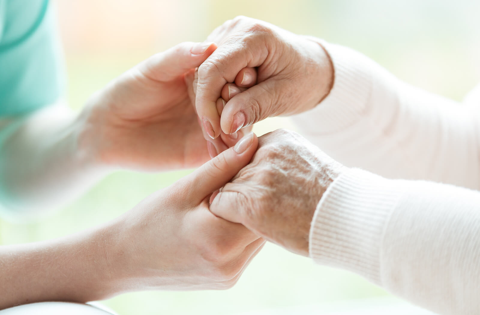 a close up photo of a young person holding the hands of a senior in support