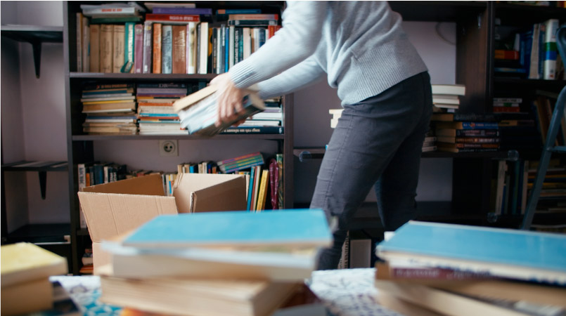 A woman is packing books from her large library into moving boxes.