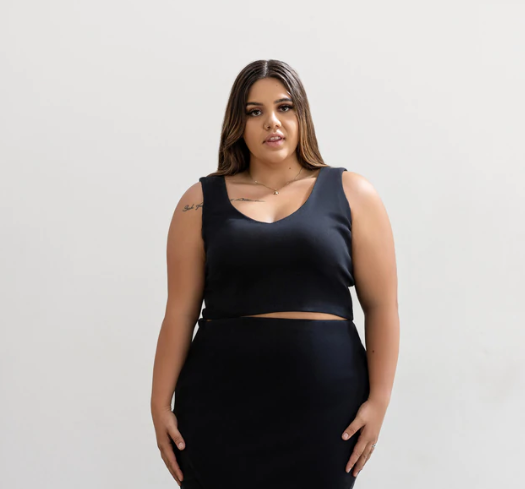 Plus size woman facing forward wearing a black tank top and black bottoms, hands at sides.