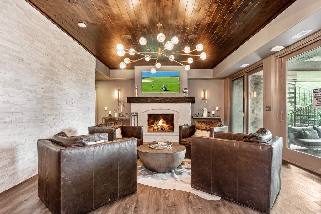 Elegant basement sitting room with fireplace, stone tile walls, wood ceiling and luxury vinyl plank flooring.
