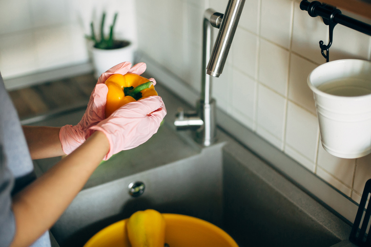 gloved hands wash a yellow pepper in the sink
