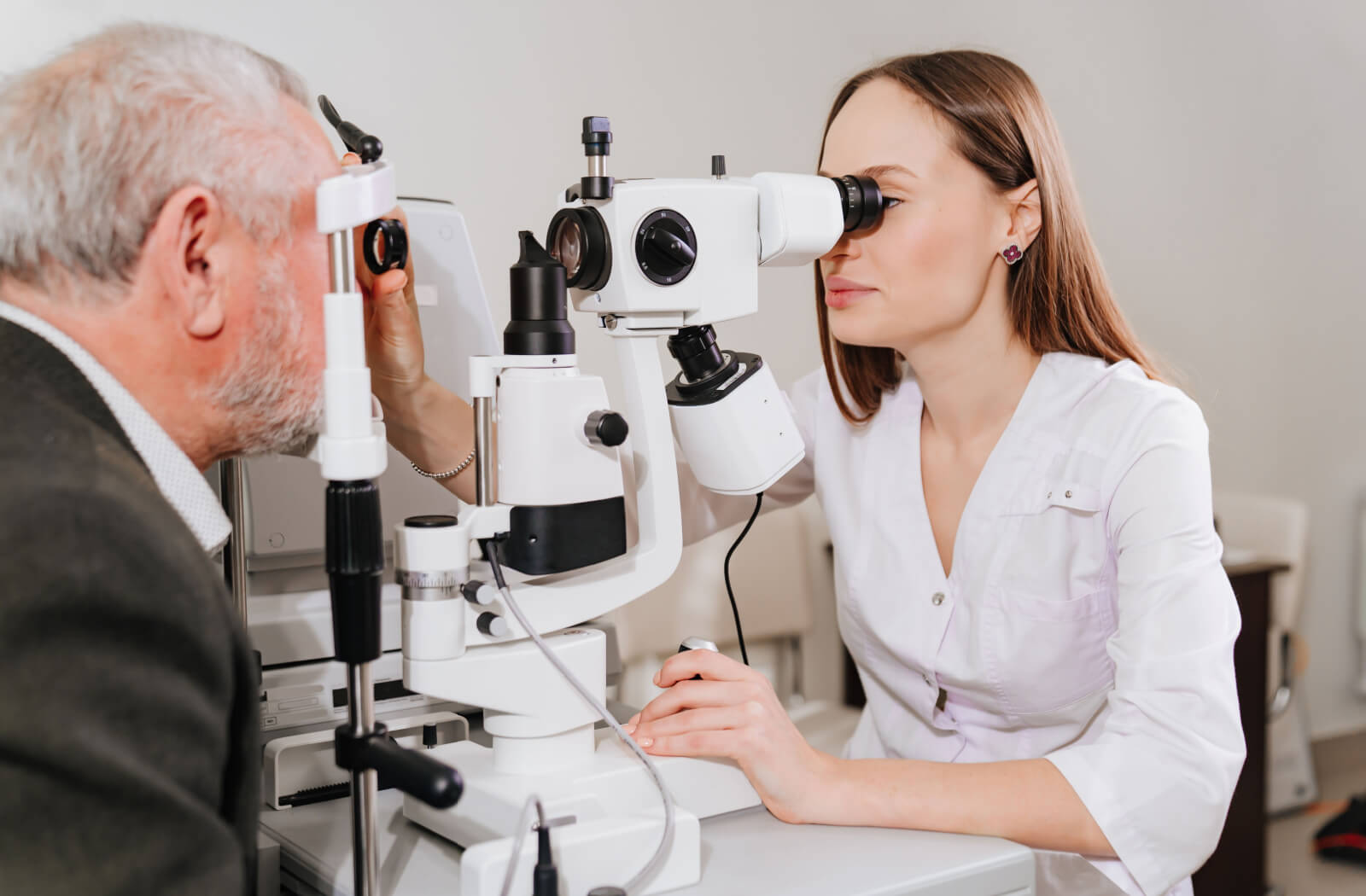A female optometrist looking into a medical device to perform an eye exam on a senior man