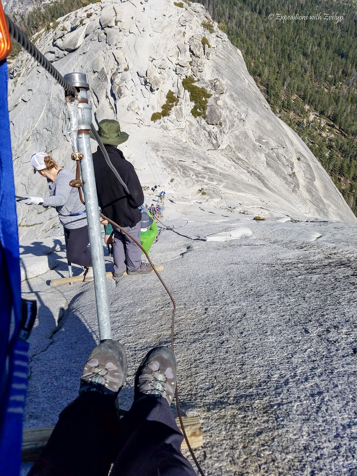 A birds eye view of descending the Half Dome Cables., steel poles that hold up steel cables for hikers to grip.  On the slick granite ground, wooden beams provide traction at intervals.