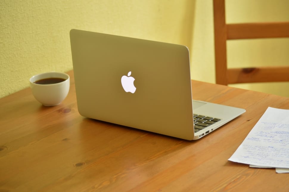 This image shows that Apple MacBook in the table with a Coffee cup and papers.