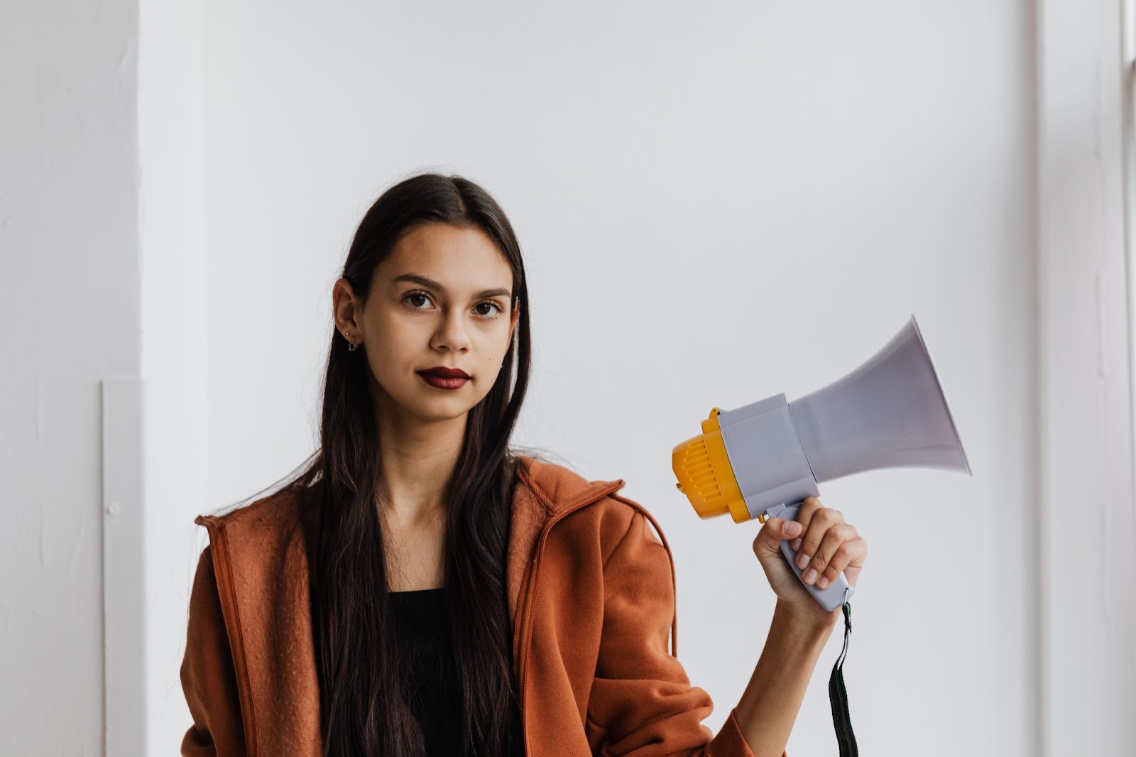 Une femme tenant un mégaphone regarde calmement et délibérément le spectateur.