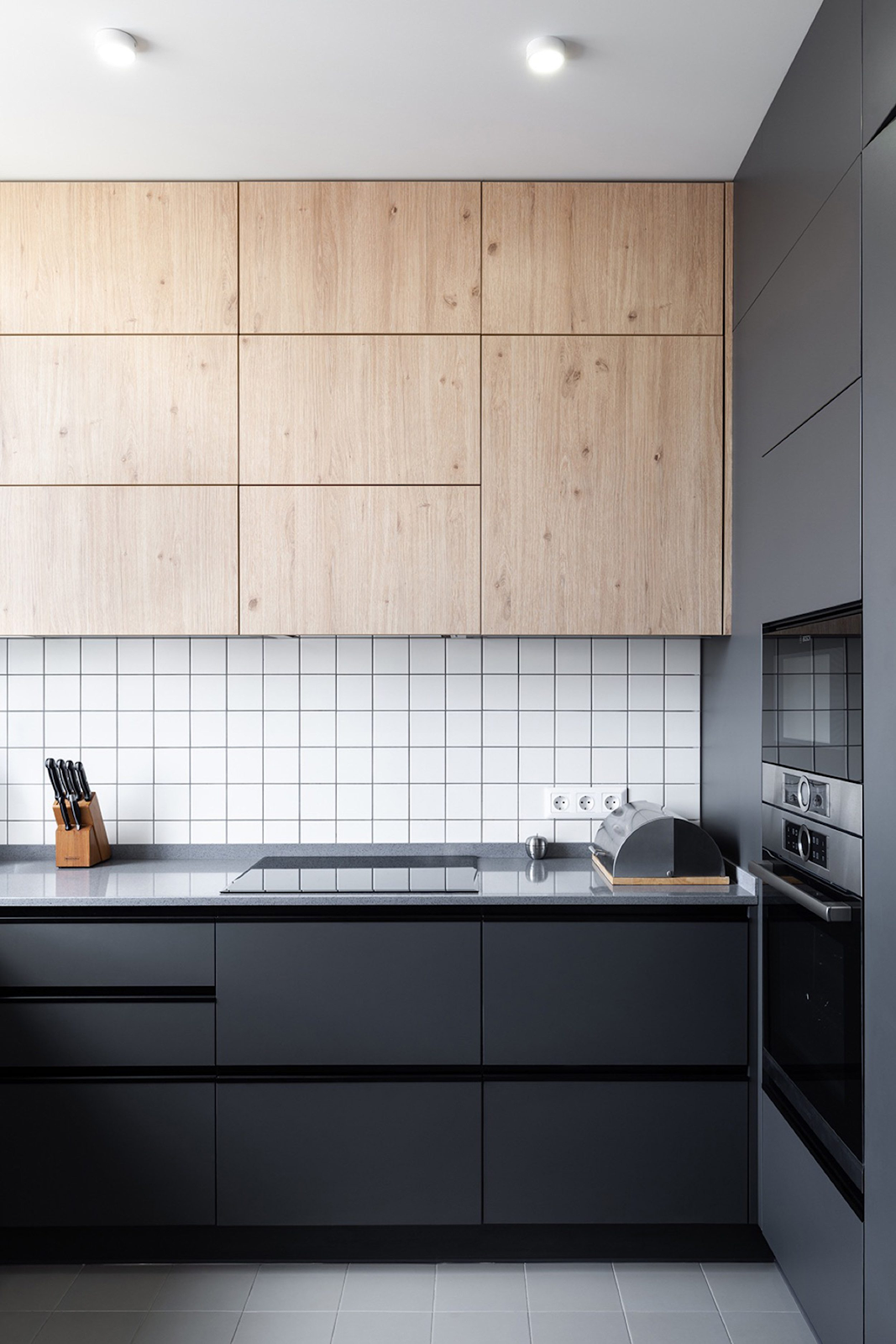 ultra modern kitchen with matte black and wood grain cabinets. clean lines and neutral colors make this kitchen feel calming and clean. the cabinets reach the ceiling for extra storage space