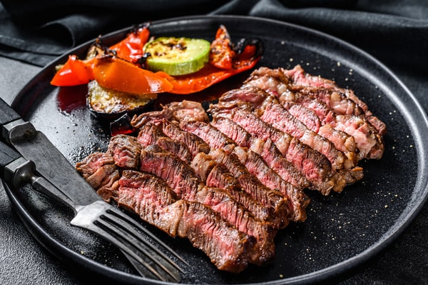 Sliced chuck steak with grilled veggies on the side, served on a black plate