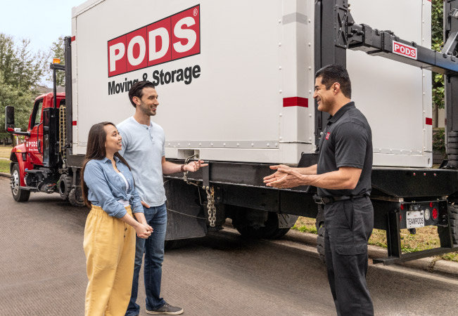 A couple discusses their move to San Diego with a PODS driver. They’re standing beside his truck which is already loaded up with their PODS portable moving container.