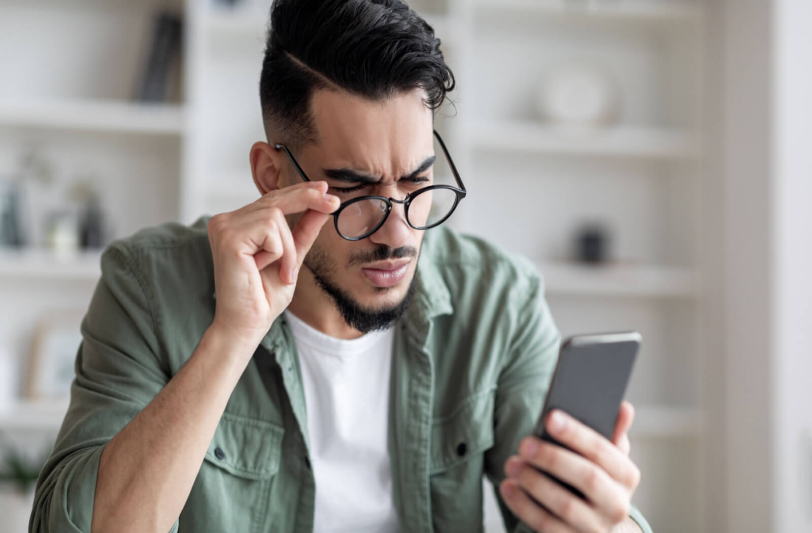 a man squints at his cellphone while wearing glasses because his prescription has changed