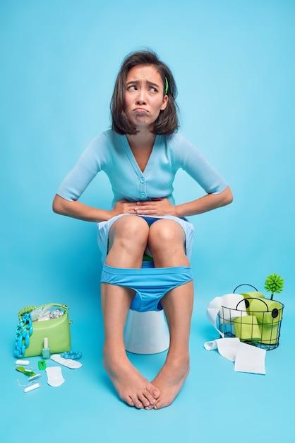 Free photo indoor shot of displeased asian woman suffers from stomachache indigestion or diarrhea poses poses toilet bowl feels unwell because of abdominal pain wears panties down on legs
