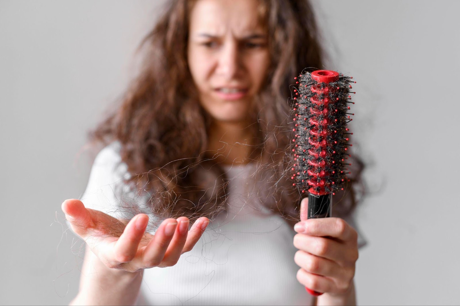 Mulher segurando uma escova de cabelo na mão, com fios de cabelos que caíram