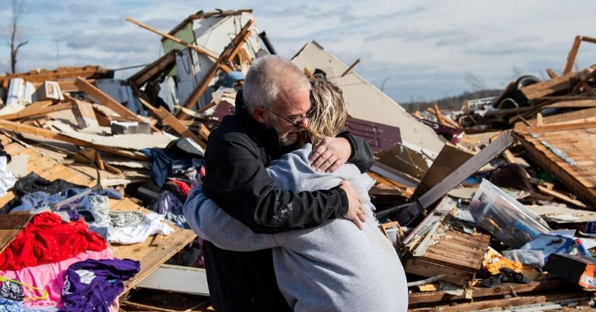 A distraught man hugs his daughter in front of collapsed walls and scattered debris from their destroyed house by a tornado.