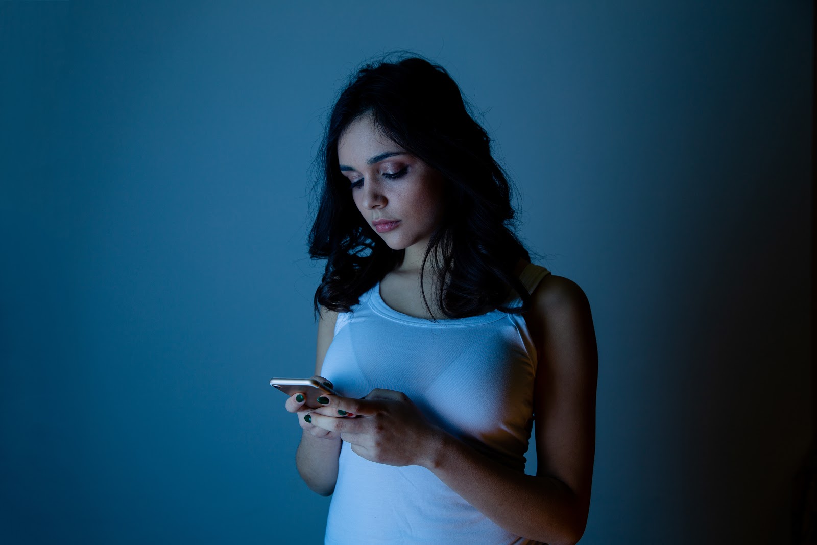 A woman in a dark room looking at her cell phone, sad