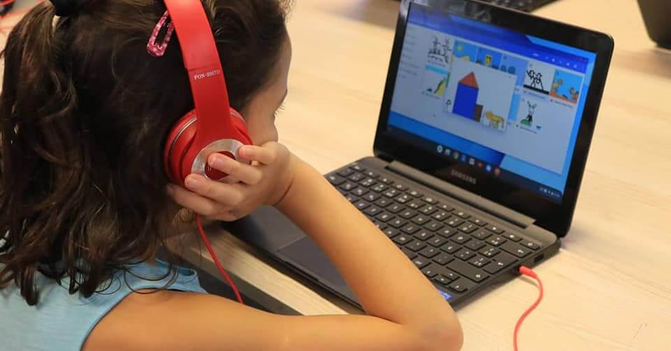 A imagem mostra uma crianças de fone de ouvidos em frente a um notebook.