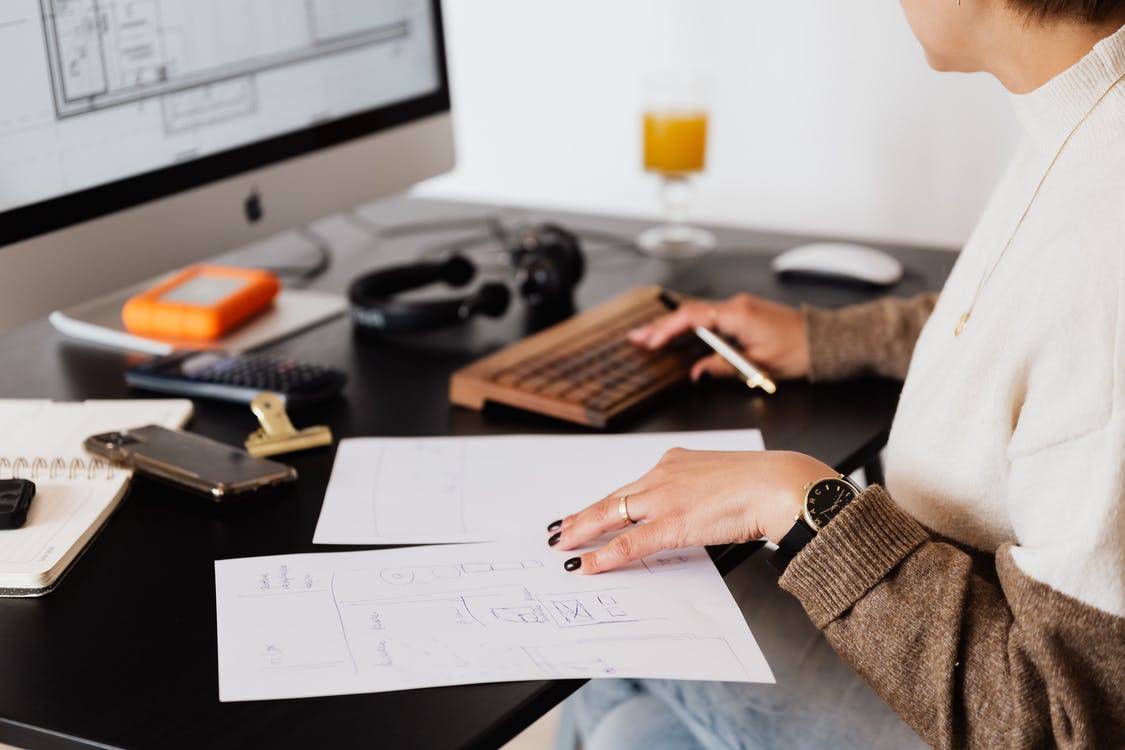 Side view of crop faceless female entrepreneur checking document and typing on keyboard of computer during work in office