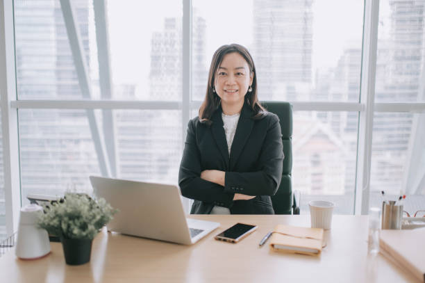 Asian chinese beautiful woman ceo senior management looking at camera smiling at her desk in office Asian chinese beautiful woman ceo senior management looking at camera smiling at her desk in office office space stock pictures, royalty-free photos & images