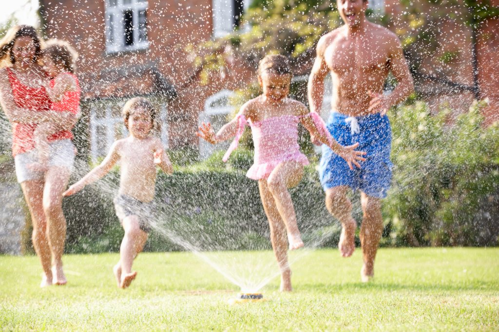 Family Running Through Garden Sprinkler