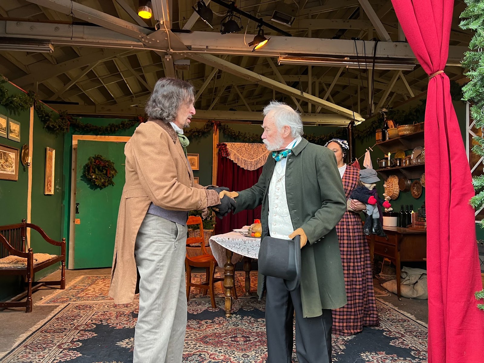 On stage, a man dressed as Dickensian Bob Cratchit shakes hands with another man dressed as Ebenezer Scrooge.