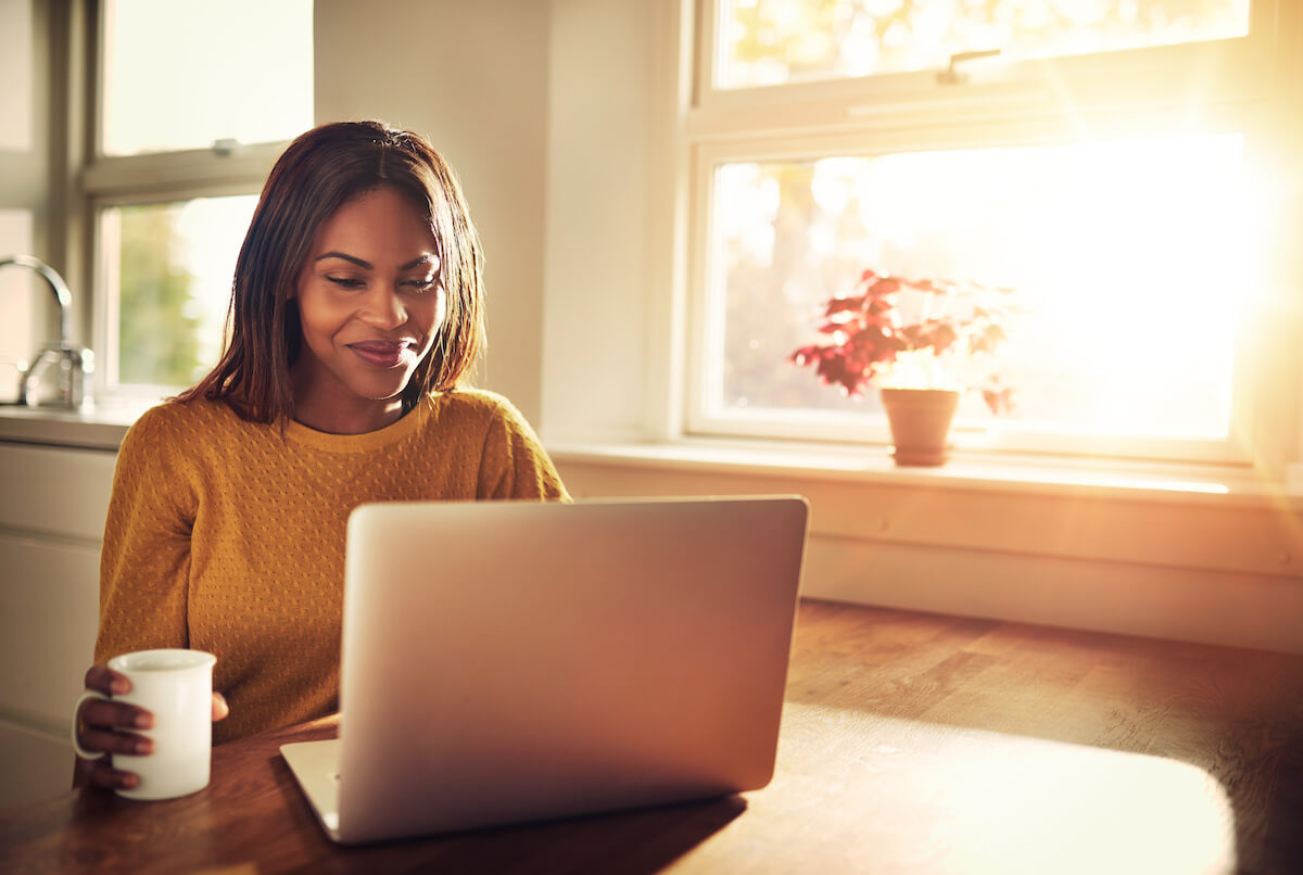 Woman holding a cup while happily reading from her laptop