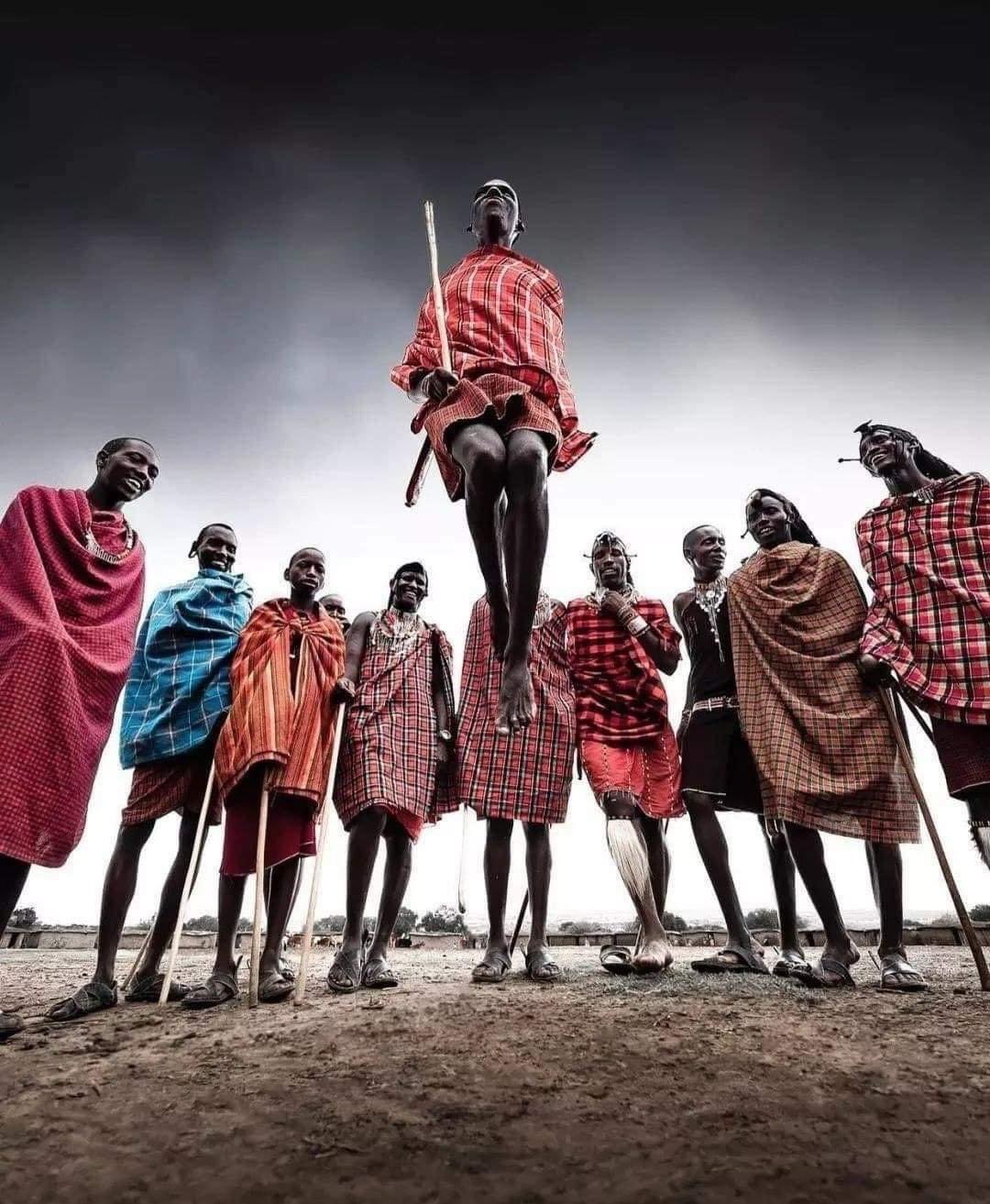 A Maasai holding a stick leaps high in the air in front of a group of other menn
