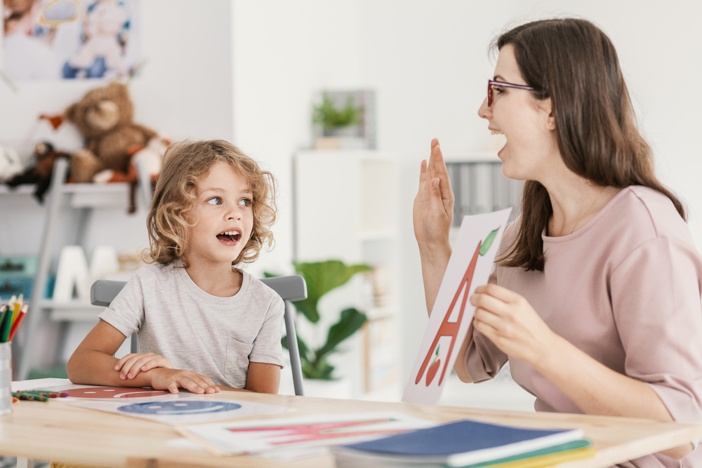 Teacher using big flash cards to teach vowels to young kid