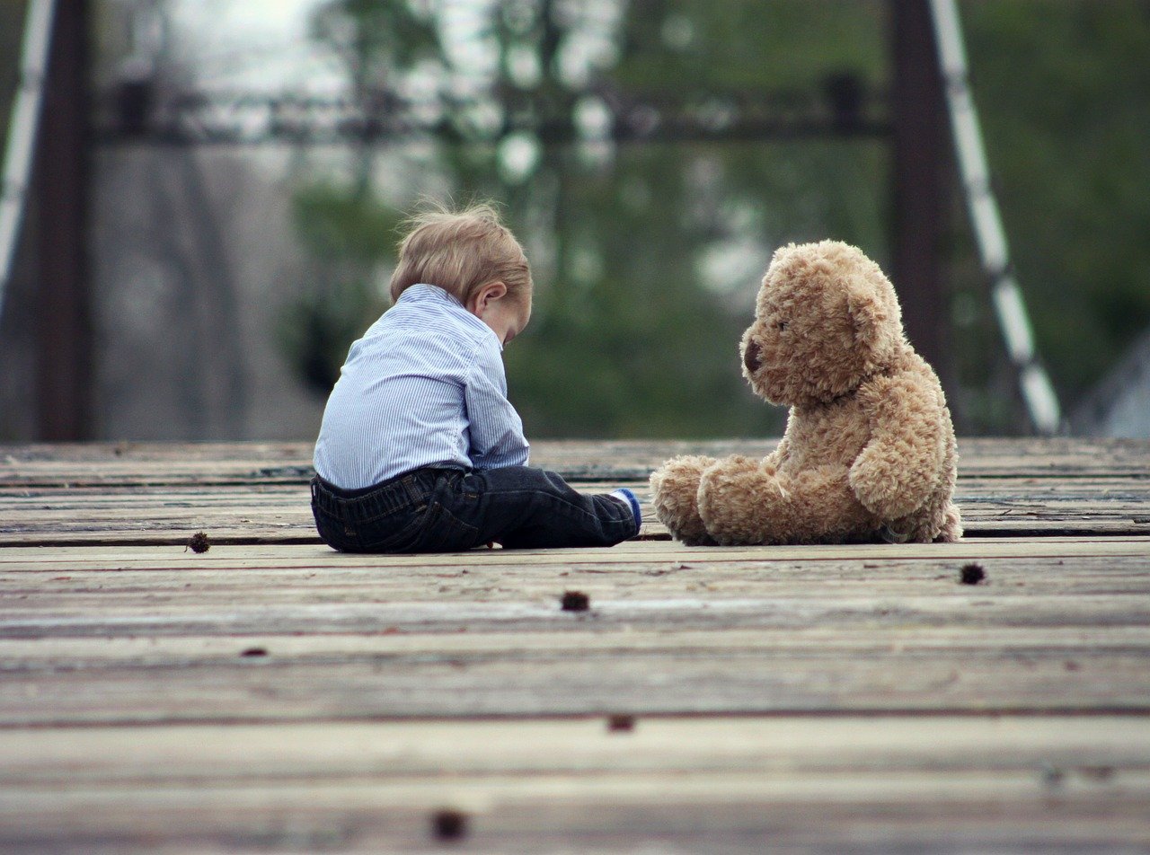 Uma criança sentada ao lado de um urso de pelúcia