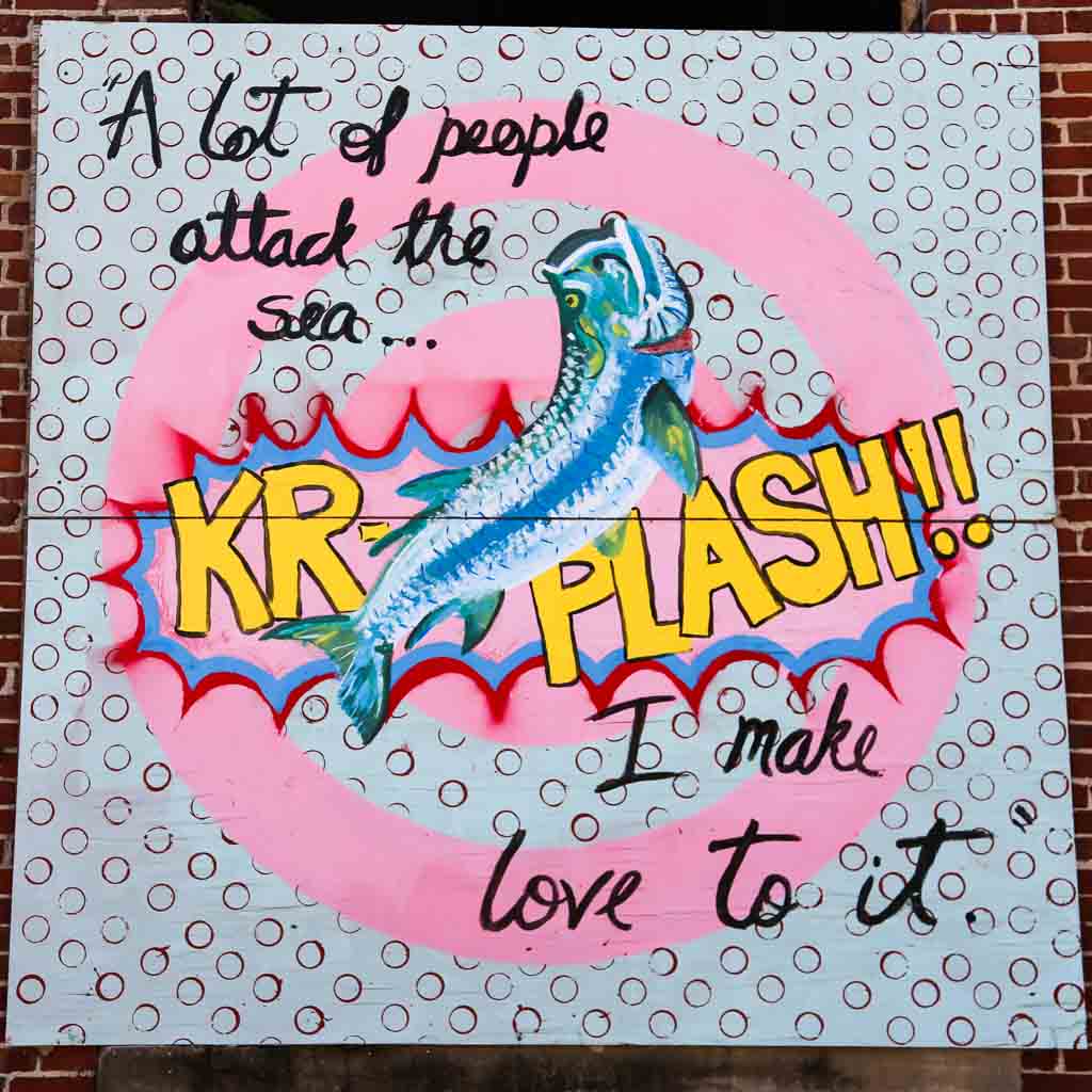 One of the street arts in Key West. It reads "A lot of people attack the sea... I make love to it." A fish with "KR-PLASH!!" behind it is in the middle of the quote. The background consists of a pink concentric circles and a grayish square with open dots.