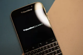 A BlackBerry phone with the words BlackBerry classic showing on the screen. The bottom half of the curved rectangular shaped smartphone has a physical keyboard