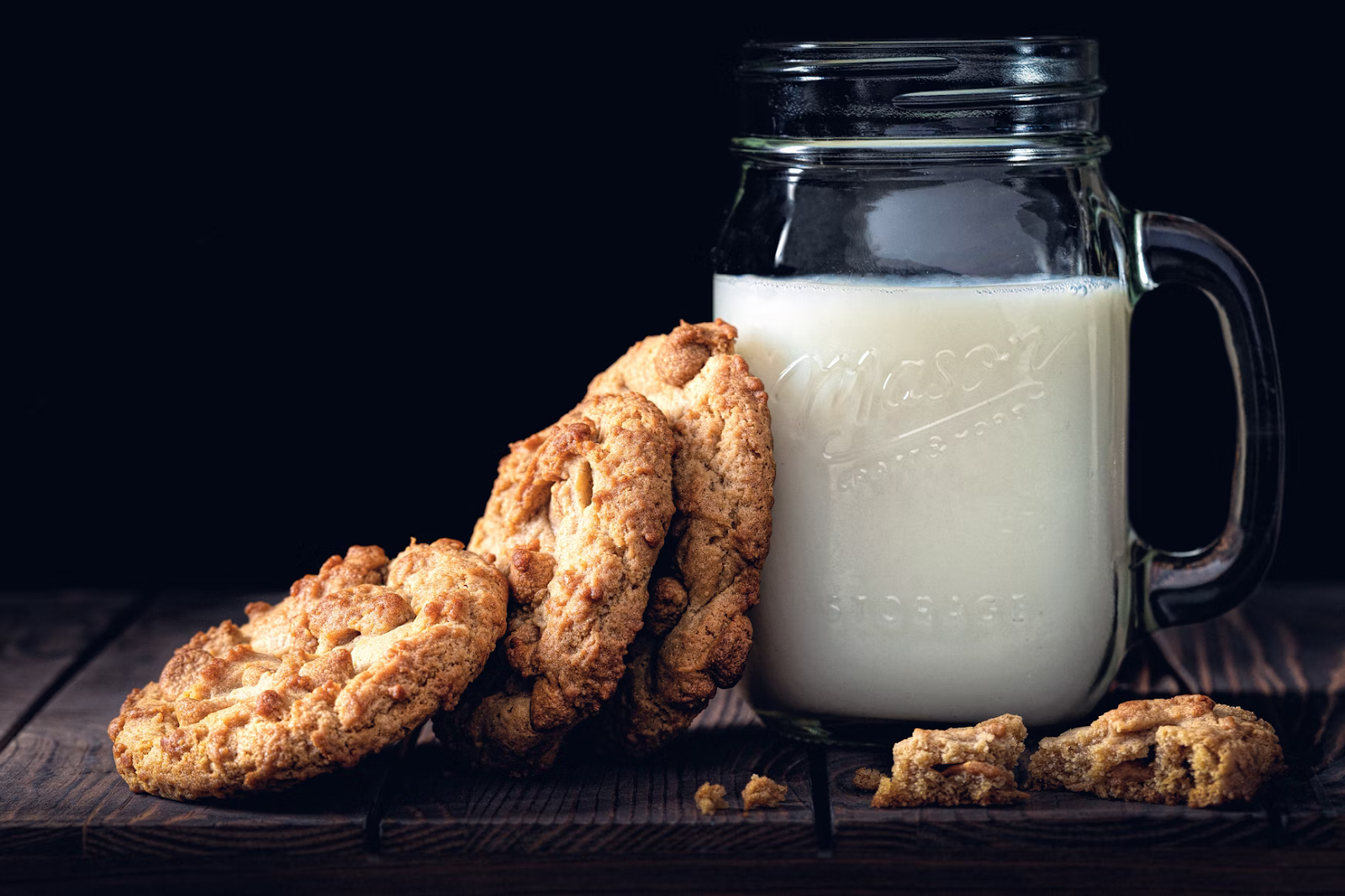 a mason jar of milk with a stack of cookies on a wooden board