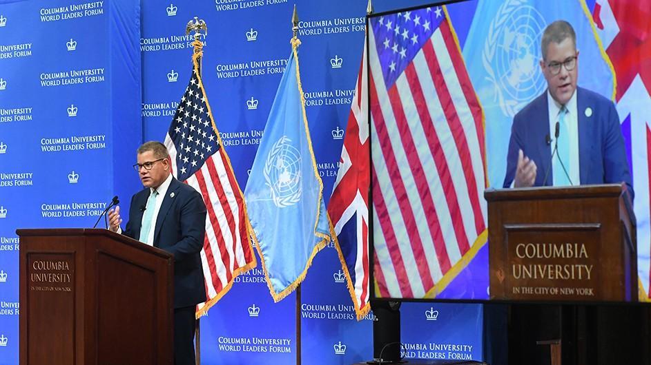 COP26 President Alok Sharma in navy blue suit speaks at a podium with Columbia signage and banner in front of U.N, U.S., and British flags on stage at Columbia University Low Library.