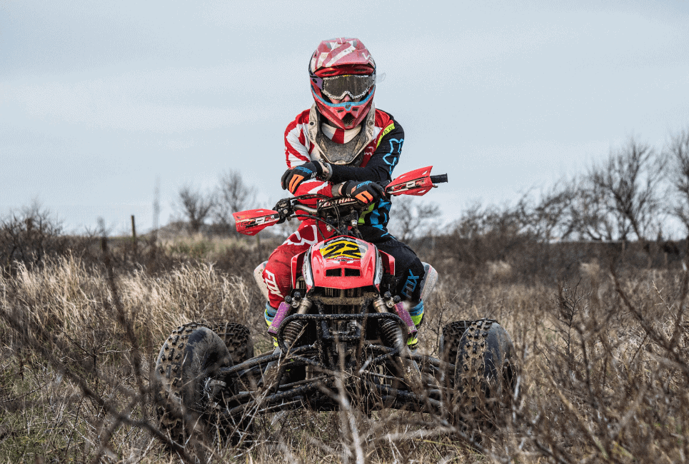 ATV rider in full gear takes a break in the midst of a scenic thicket, ready to continue the off-road adventure