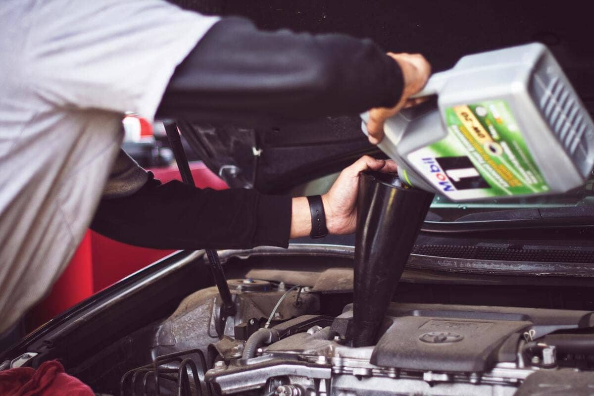 Un meccanico che sta mettendo dell'olio all'interno di un motore di un auto