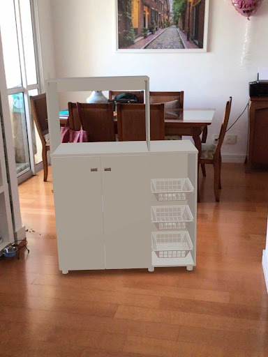 Foto de um modelo 3D representando um móvel branco em uma sala com outros móveis físicos. O modelo 3D projetado em Realidade Aumentada ainda sem sombra.