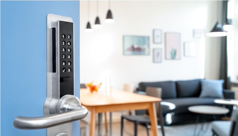 The first view of a short-term rental after using a keypad to open the front exterior door. The side of the door with the keypad and handle is in view, and the living room/dining room combo is blurred out in the background, showcasing a couch, dining table, collage of framed pictures, and other typical features of a small apartment.