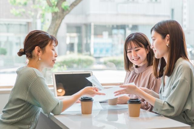 カフェで話をしている3人の女性の写真。紙を手に、会議を行っている様子。