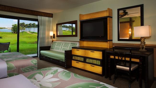 Two queen beds across from a desk, TV-dresser, daybed and, beyond, a patio and Seven Seas Lagoon