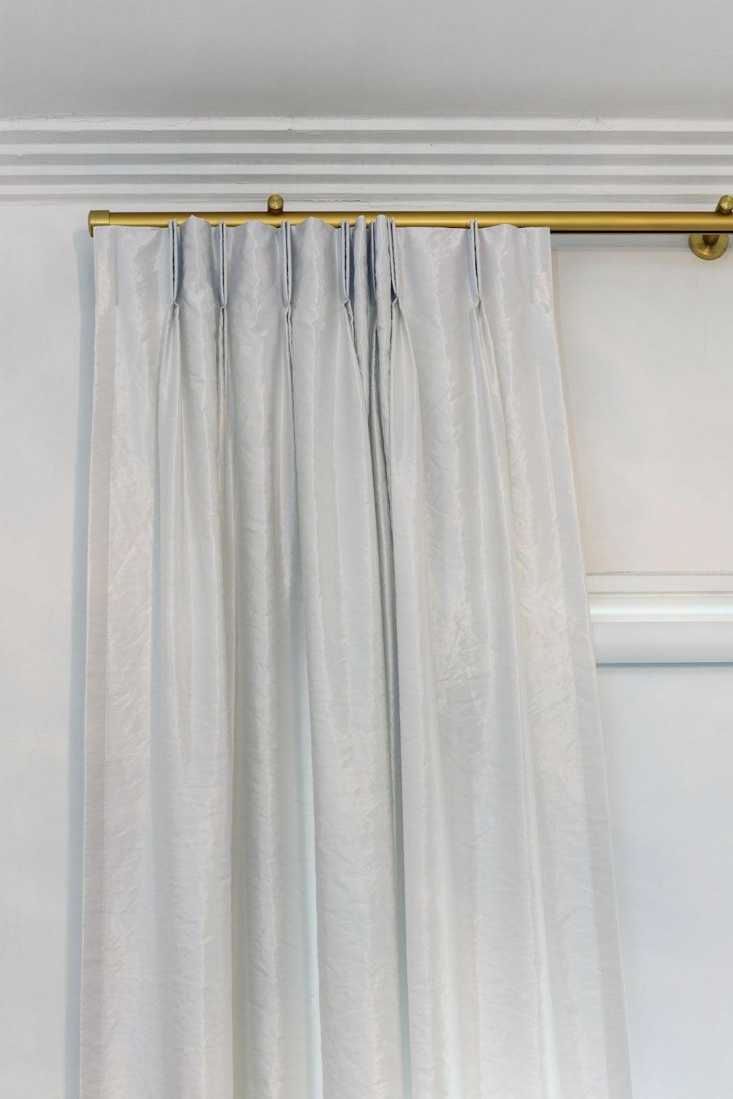White pleated curtains hanging from a gold curtain rod
