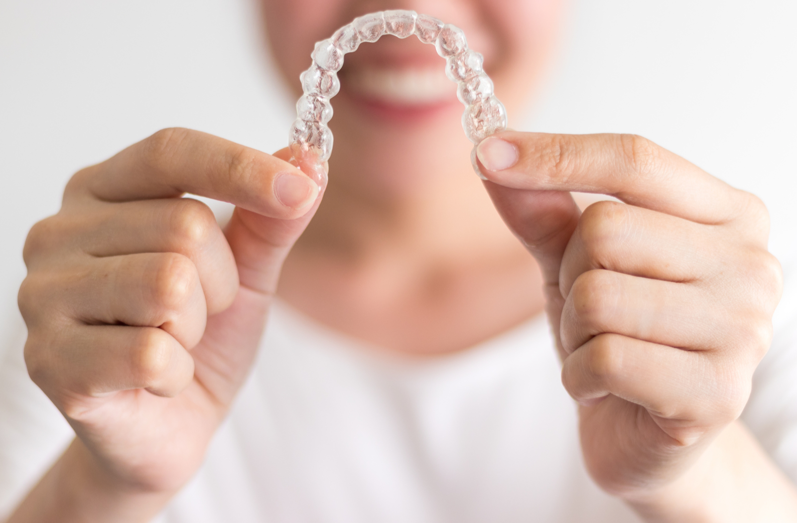 lady smiling out of focus holding a clear plastic aligner with both hands