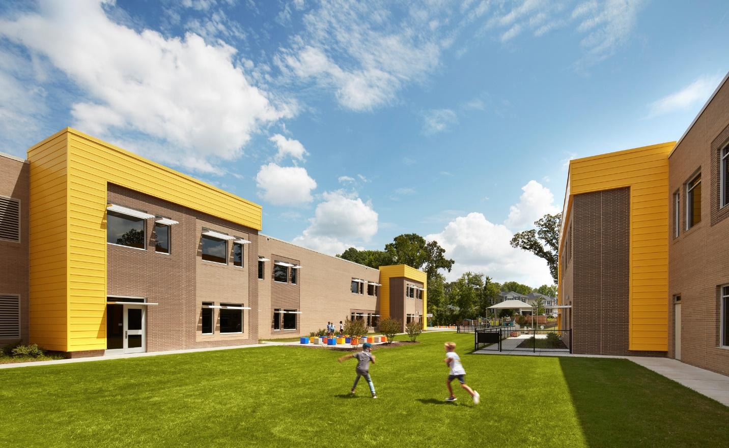 A picture containing grass, sky, building, outdoor with kids running around the school.