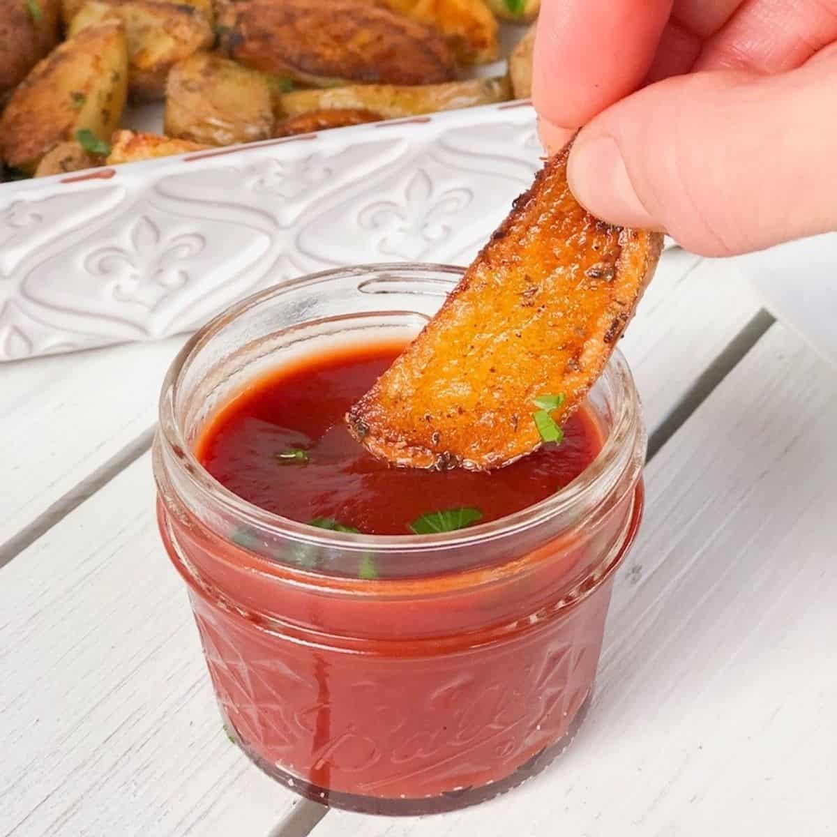 Crispy baked potato wedge being dipped into ketchup.