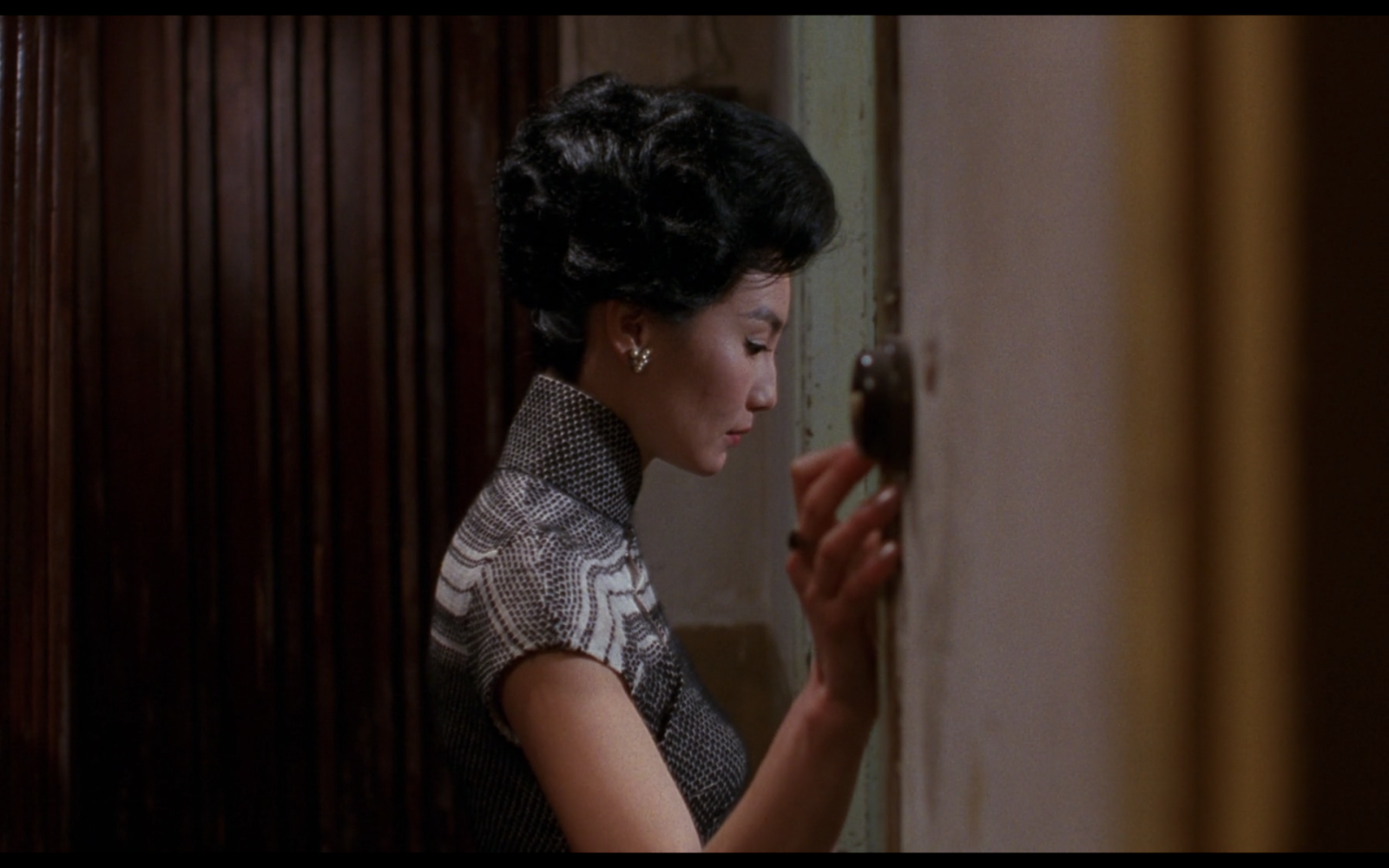 A screen still from the film In the Mood for Love, featuring Mrs. Chan as she enters a doorway into a room we cannot see.