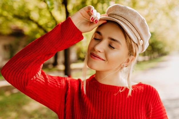 Portrait of a beautiful blonde girl in nice red sweater and light hat posing in the autumn park. Free Photo