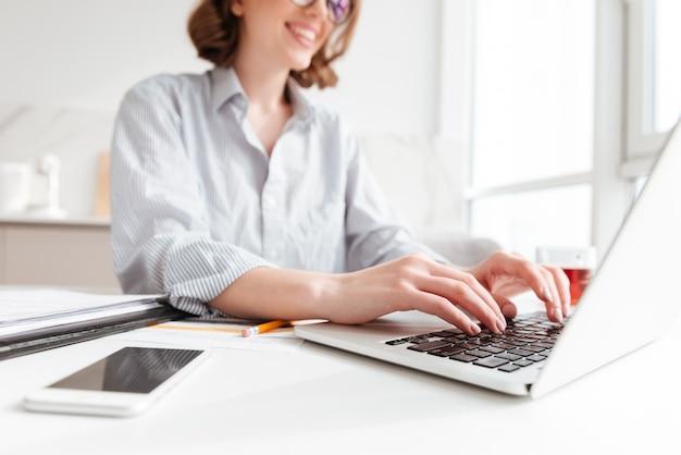 Free photo brunette woman typing email on laptop computer while sitting at home, selective focus on hand