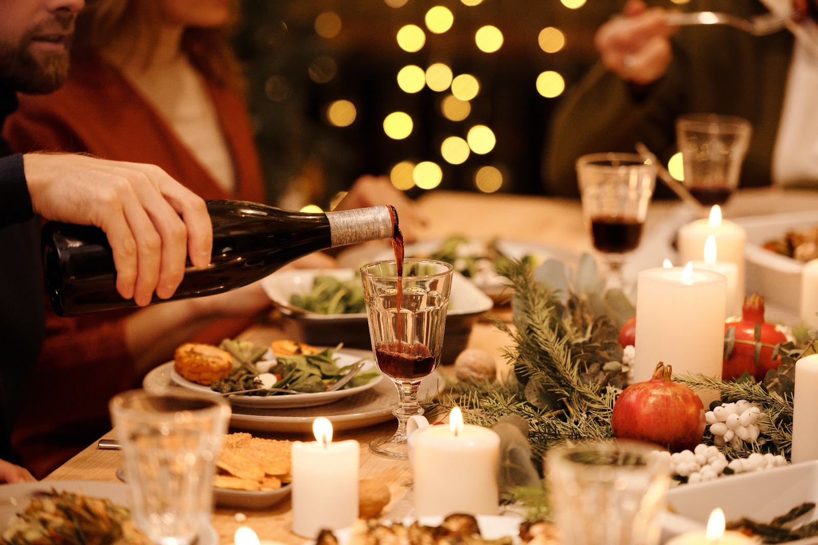 a person's hand pouring red wine into a glass at a festive dinner table