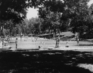 A wide photo of folks standing by the historic Deep Eddy Pool with lots of tree coverage. 