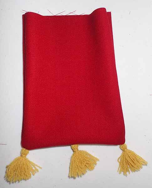 The outer layer of a red wool bad, top edge unfinished, with three gold tassels on the bottom.