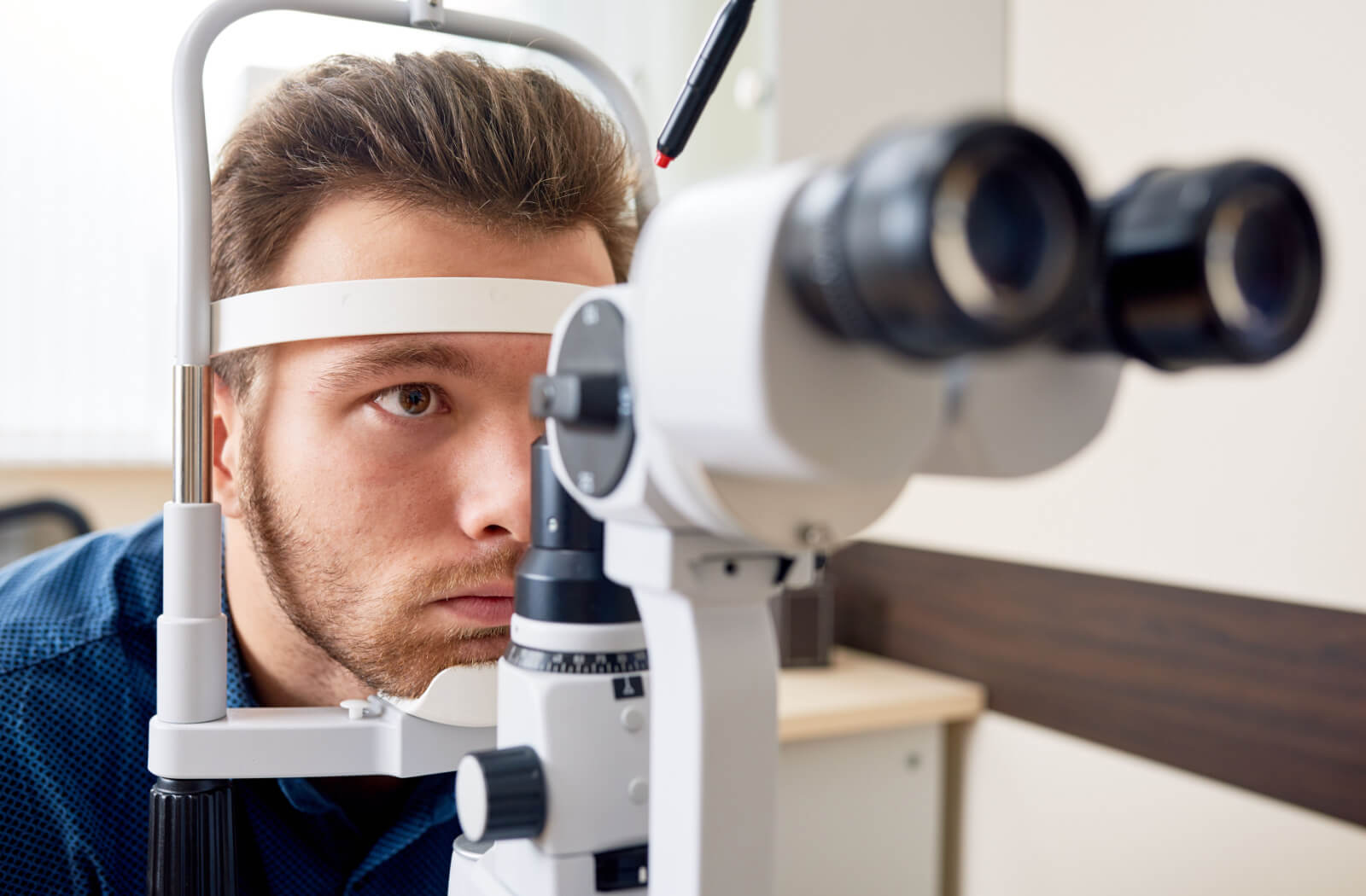 A man sitting in an optometrist's office and looking into a machine that tests his vision.