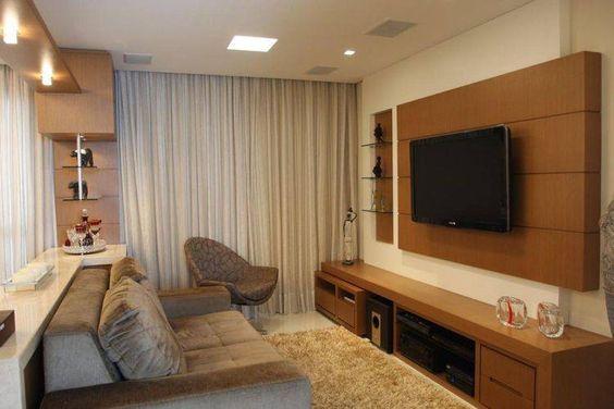 Sala com Painel para TV que reproduz madeira harmonizando com rack, sofá e poltrona cinzas, tapete e cortina longa.
