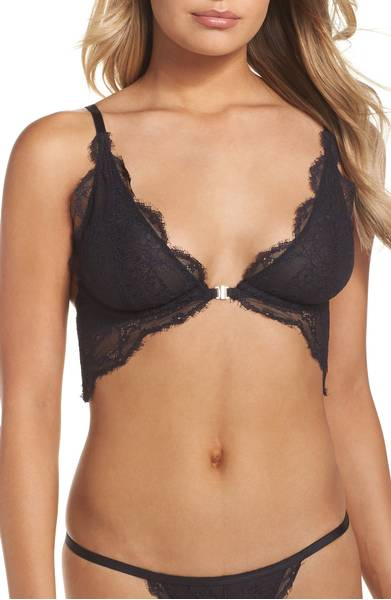 A woman wearing a black lace bralette with floral patterns and thin straps, paired with matching lace underwear. The mood is elegant and intimate.