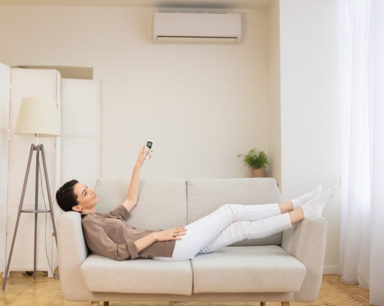 A lady lying on a sofa turning on the AC unit